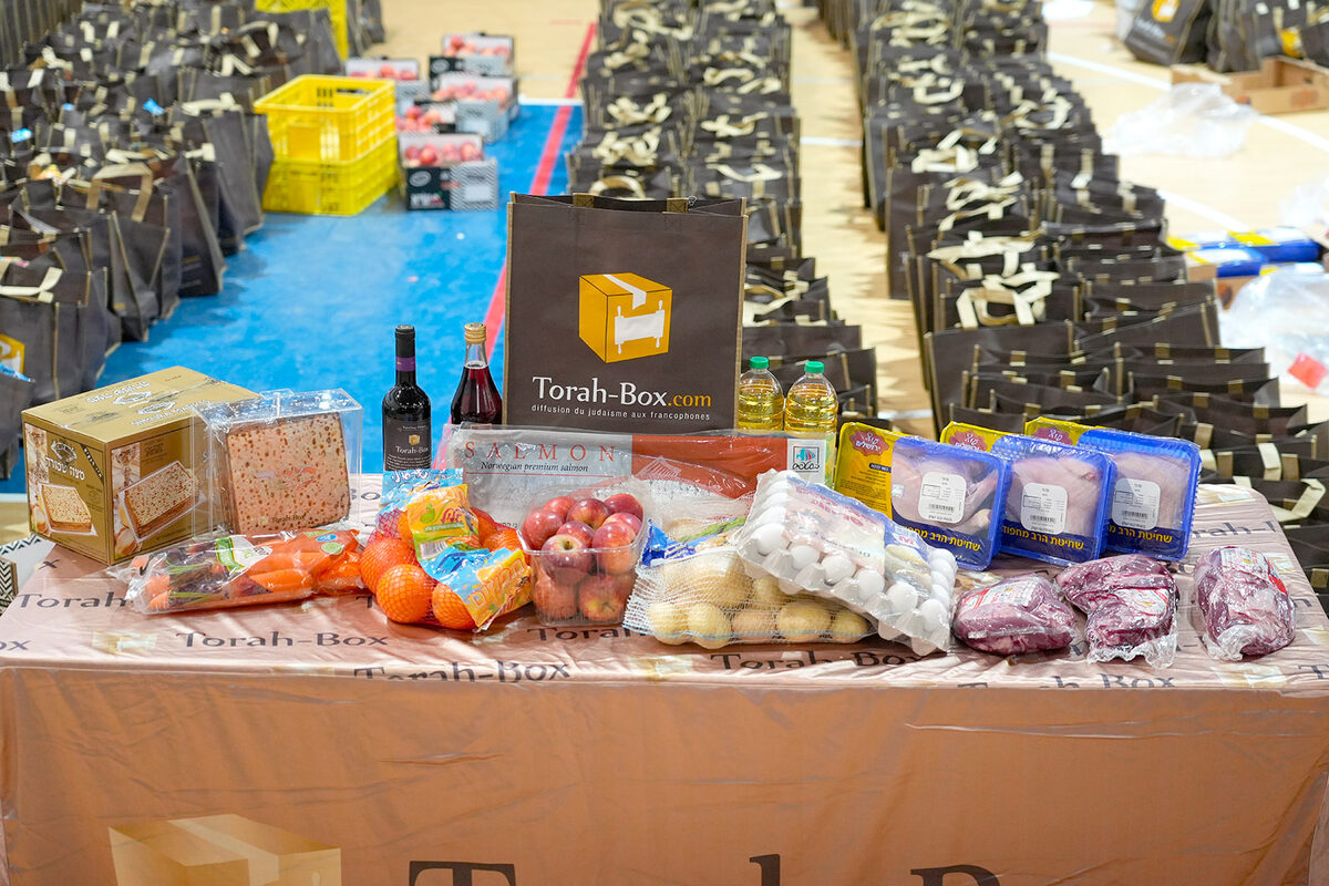 Colis alimentaires Torah-Box pr&eacute;par&eacute;s pour les f&ecirc;tes, align&eacute;s dans un gymnase